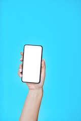 Female hand holding and showing smartphone with blank white screen isolated on blue background.