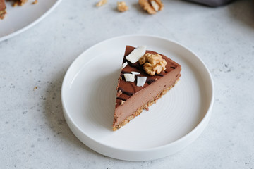 Piece of homemade chocolate raw vegan cake - healthy dessert made from coconut milk, butter, cashew, cacao, walnut