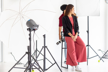 Young photographer shooting young beautiful female model posing for a photo shoot in studio with a digital camera