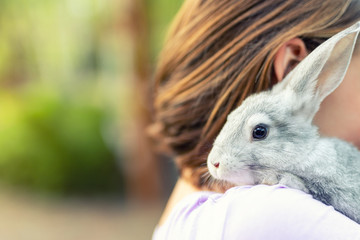Cute adorable sweet little rabbit sitting on shoulder of young adult brunette woman at warm sunset time country outdoors. Animal friendship and care concept