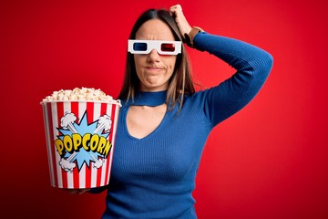 Young blonde woman wearing 3d glasses and eating pack of popcorn watching a movie on cinema confuse and wondering about question. Uncertain with doubt, thinking with hand on head. Pensive concept.