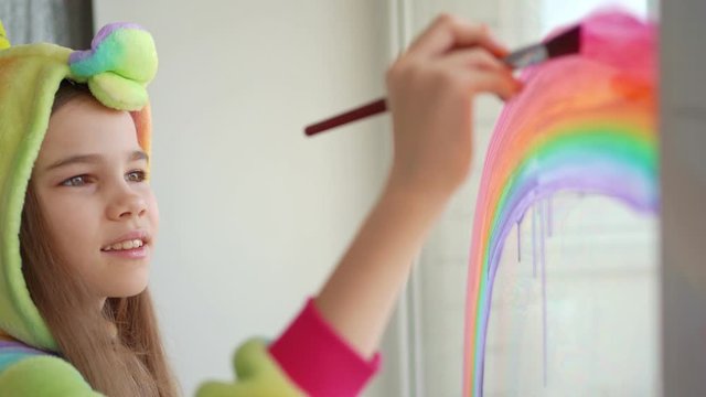 teen girl in kigurumi draws rainbow on window.