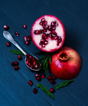 Sliced Pomegranate on a black background with seeds in a spoon and mint