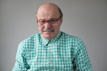 Obraz premium Sick sad hidpsnic man in glasses is tired to be alone feeling stressed. Negative facial human emotion on grey wall.