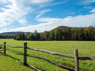 Fototapeta na wymiar Landscape nature scene in the Laurel Highlands of Pennsylvania with a fence in the foreground and a meadow and tree line in the background with bright blue cloudy skies!