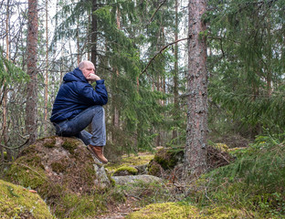 Naklejka na ściany i meble A man alone sits on a stone in the forest and thinks. Solitude in nature calm and relaxation.