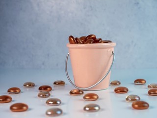 Peach ceramic bucket filled with orange glass marbles on a white counter with a gray plaster background.