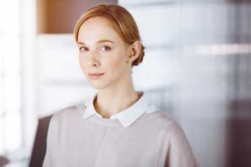 Friendly adult casual dressed business woman standing straight. Concept of a business headshot or portrait in office