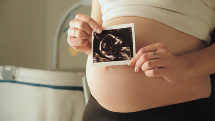 Pregnant woman middle body section holding the echography photograph of her baby in front of her belly. © CameraCraft