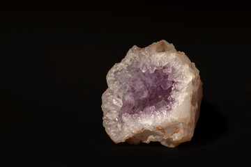 Untreated mineral amethyst quartz is a soft lilac color, isolated on a black background. Semiprecious stone. House decoration