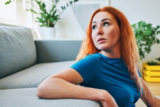 Worried young woman looking through the window at home