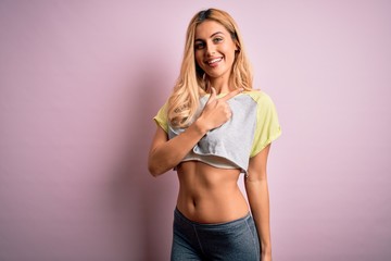 Fototapeta na wymiar Young beautiful blonde sportswoman doing sport wearing sportswear over pink background cheerful with a smile of face pointing with hand and finger up to the side with happy and natural expression