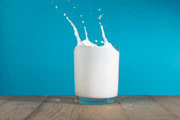 Splash of milk from the glass on wooden table. Fresh milk splash in glass on blue background