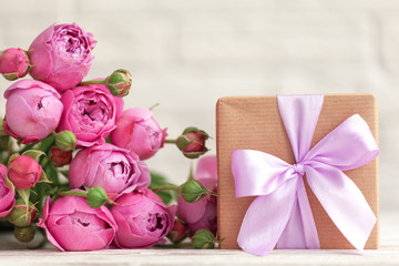 Gift box wrapped with craft paper and pink bow on pink roses background. Mother day concept.