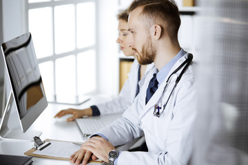 Red-bearded doctor with female colleague discussing current disease therapy while sitting at...