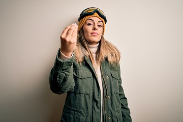 Young brunette skier woman wearing snow clothes and ski goggles over white background Doing Italian gesture with hand and fingers confident expression