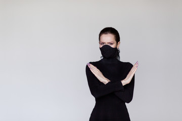 Obraz na płótnie Canvas stop coronavirus concept. Girl in a black protective medical mask shows a ban sign. Stylish. Covid-19 quarantine.