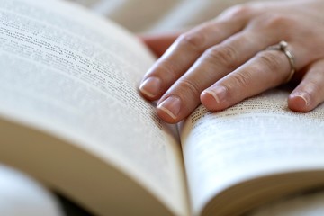 Fototapeta premium A close up portrait of a hand of a person touching the page in a book where she is reading it. The person fell asleep whilst reading and the hand is still holding the book open.