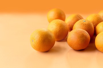 A portrait of multiple fresh oranges filled with vitamin c. The healthy pieces of fruit are displayed on an orange background.