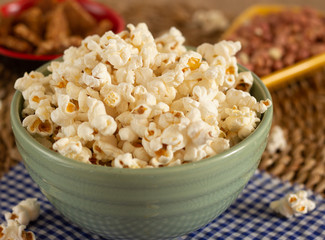 big bowl full of popcorn  surrounding by peanuts candies on the straw background