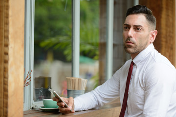 Fototapeta premium Portrait of businessman thinking while using phone at the coffee shop