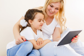 Fototapeta na wymiar Happy family mom and kid daughter using digital tablet sitting on sofa, smiling parent mother with child girl holding tablet looking at screen do online shopping make video call watch cartoons