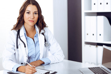 Doctor woman filling up medical form while sitting at the desk in hospital office. Physician at work. Medicine and health care concept