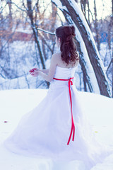 Fototapeta premium Snow White princess with the famous red apple. Fairy tale tale concept with poisoned bitten red apple. Once upon a time. Portrait of beautiful girl in white dress with red ribbon in the winter forest.