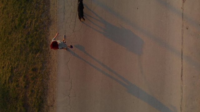 Young woman walks with her dog along asphalt road at sunset casting shadows