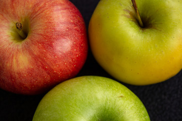 Three apples, one green and two red and yellow on a dark background