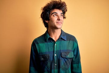 Young handsome man wearing casual shirt standing over isolated yellow background smiling looking to the side and staring away thinking.