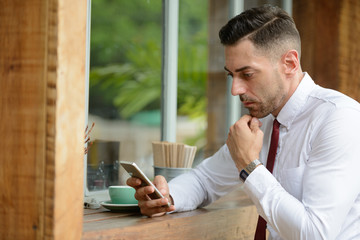 Portrait of businessman thinking while using phone at the coffee shop