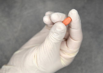 Hand in medizinischem Einweghandschuh und Medikament zwischen Daumen und Zeigefinger