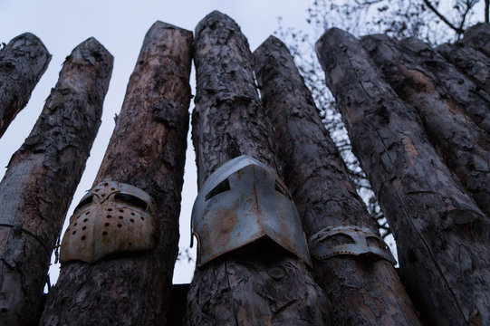 Three visors of medieval helmets are mounted on logs of a log fence