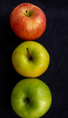 Three apples, one green and two red and yellow on a dark background