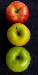 Three apples, one green and two red and yellow on a dark background