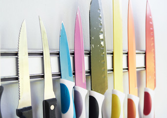 A collection of professional sharp chefs knives on a magnetic strip on a kitchen wall. Colour...