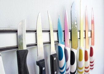 A collection of professional sharp chefs knives on a magnetic strip on a kitchen wall. Colour...