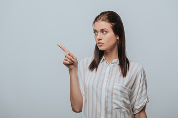 Beautiful young woman pointing with finger isolated on grey