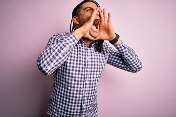 Young handsome african american afro man with dreadlocks wearing casual shirt Shouting angry out loud with hands over mouth