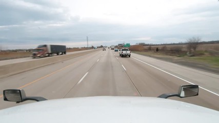 Dashcam type view of front of semi truck driving on almost empty interstate passing a Stay-at-home sign before an overpass. Very few vehicles on the road. Cloudy and bright weather conditions.