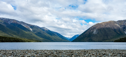 Beautiful panoramic photo of Rotoiti Lake with the pebbles shore in the foreground and the snow capped mountains in the background taken on a cloudy winter day, New Zealand