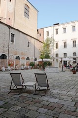 Fototapeta na wymiar Zwei Liegestühle auf dem Innenhof der Ca'Foscari Universität im Centro Storico der Lagunenstadt Venedig. Ruhiger Blick auf den gepflasterten Campo.