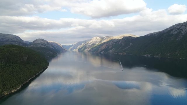 Lysebotn Fjord Norway drone stock footage by DroneRune. Drone flies high up over the fjord. Mountains on both sides. There is a boat on the river, sailing towards the drone