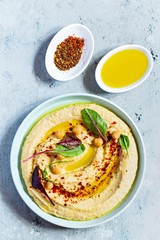 Classic hummus in a bowl with herbs, smoked paprika, olive oil and lettuce on a blue (gray) background. Healthy vegan food. A dish of Middle Eastern cuisine. Healthy eating concept.
