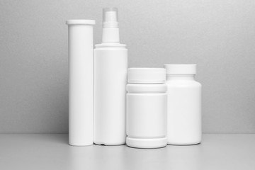 4 white jars for medicines and vitamins and dietary supplements without a name are on a gray shelf.