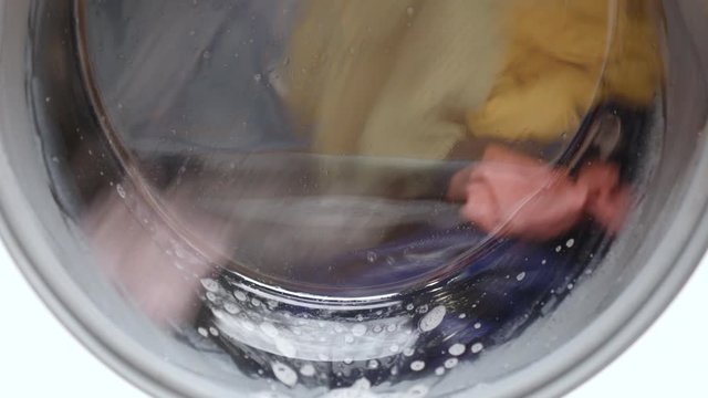 White washing machine washes dirty colorful clothes. Concept of clear, purity, health, hygiene and technologies. Close-up 4K video.