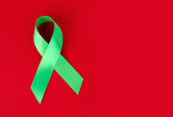 Green symbolic ribbon - the problem of organ donation, mental health. On a red background