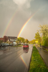 Doppelter Regenbogen spiegelt sich in regennasser Strasse