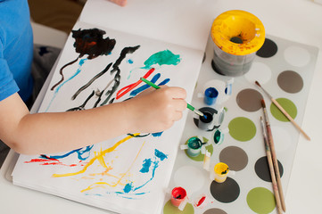 Kid's hand is painting colorful picture with gouache.